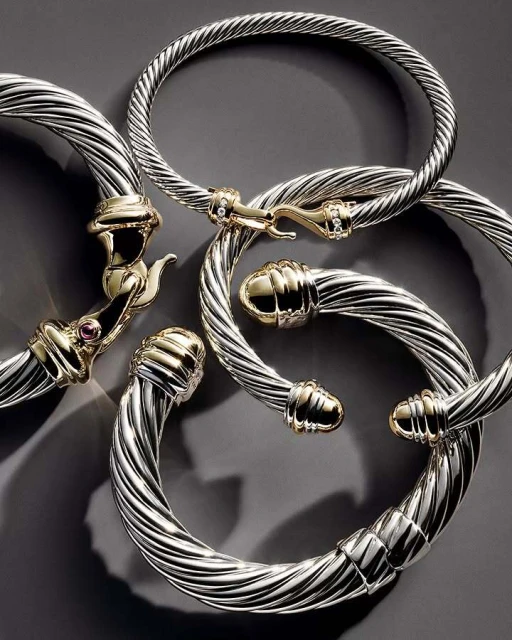 Close-up of five silver and gold cable bracelets arranged on a gray surface, showcasing their twisted designs and metallic shine.