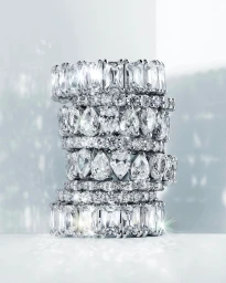 A vertical stack of multiple sparkling diamond rings with various cut stones on a bright surface.