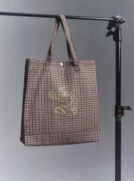 Plaid tote bag hanging from a black metal garment rack against a neutral grey studio backdrop