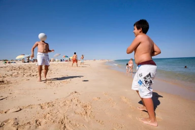 Two boys playing on a sunny sandy beach with blue ocean and clear sky, photographed by Emile Luider.