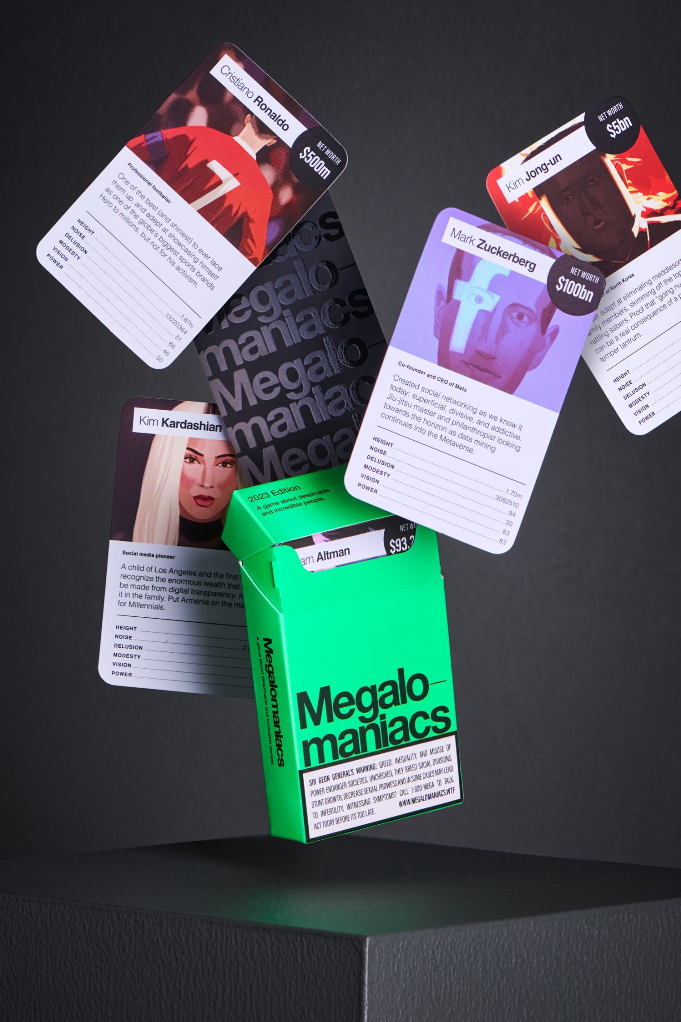 Green pack of Megalomaniacs cards and celebrity cards floating in the air on top of a gray geometric base against a dark gray background.