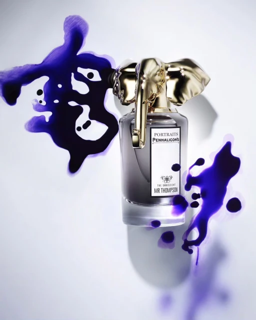 Elegant perfume bottle with a gold elephant stopper and purple ink splashes creating a luxurious and artistic beauty product still life.