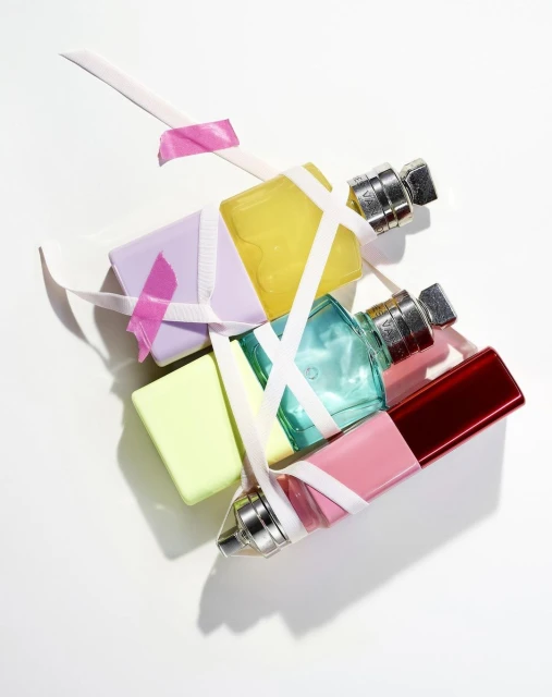 Overhead studio shot of perfume bottles and soap bars in pastel colors, arranged and taped together with white ribbons on white background.