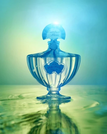 Elegant Guerlain Shalimar perfume bottle in a studio setting with a reflective surface and vibrant blue and yellow gradient lighting.