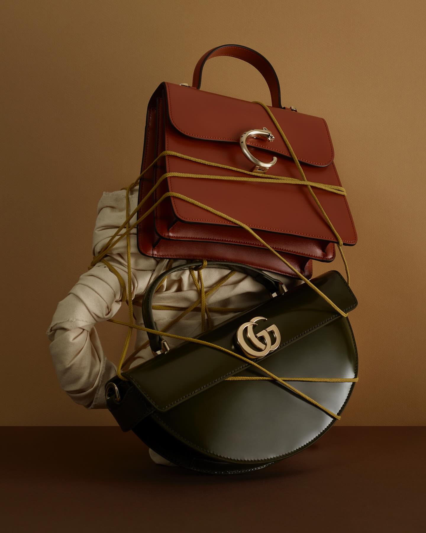 Elegant fashion still life featuring a stack of luxury handbags, wrapped with string against a tan background, showcasing high-end accessories.