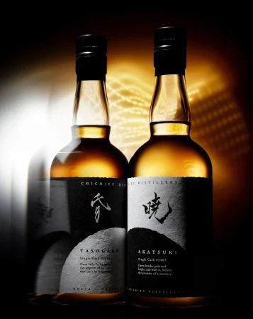 Two bottles of Chichibu distillery whiskey with black caps and labels with Japanese calligraphy, highlighted in a dark setting.