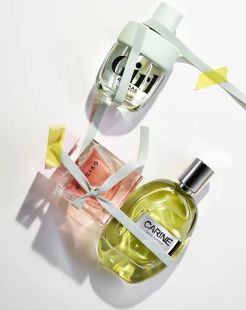Three perfume bottles of different shapes and colors are arranged on a white surface, adorned with pastel-colored ribbons and tape.