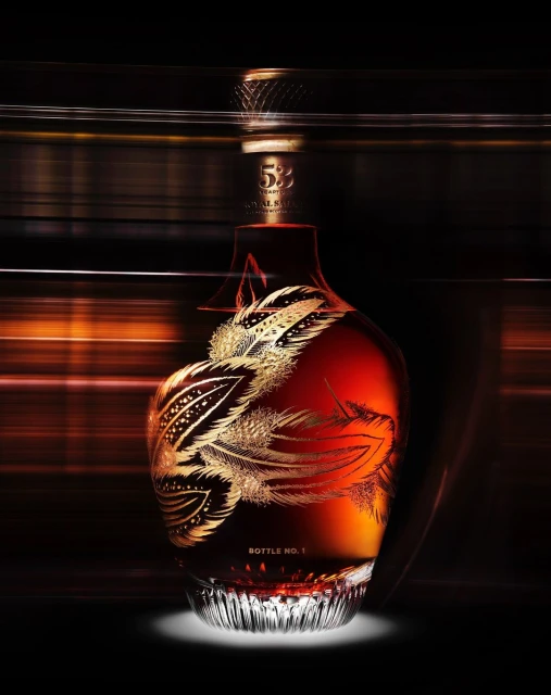 Elegant decanter of amber liquid with golden feather motif against a blurred background, showcasing sophisticated bottle design.