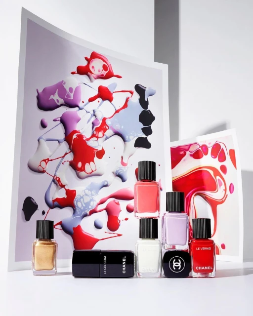 Colorful nail polish bottles and abstract paint swatches on white backdrop, product shot for beauty or fashion editorial use.