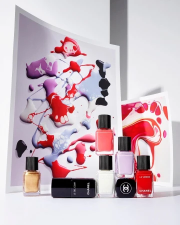 Colorful nail polish bottles and abstract paint swatches on white backdrop, product shot for beauty or fashion editorial use.