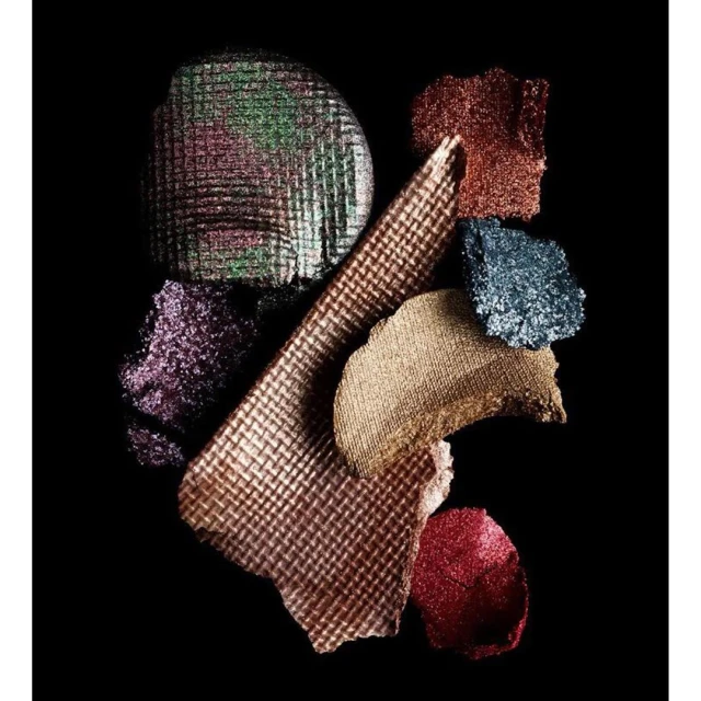 Assorted pressed pigment eyeshadow swatches with multiple textures and glitter on a black background, close-up studio product shot.