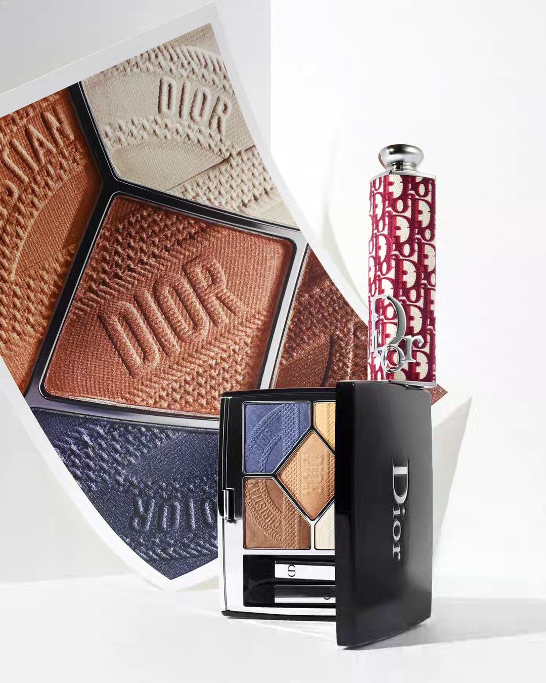 Dior eyeshadow palette open on a white surface with a lipstick tube and a printed image insert in the background.