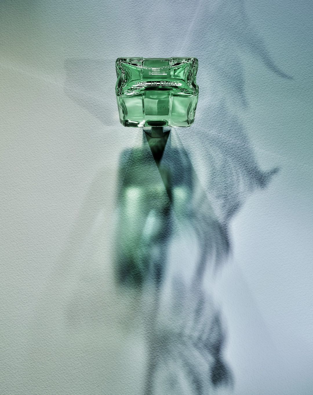 An eye-level product shot captures a green glass jar casting dramatic shadows against a subtly textured, gradient white-to-blue backdrop.