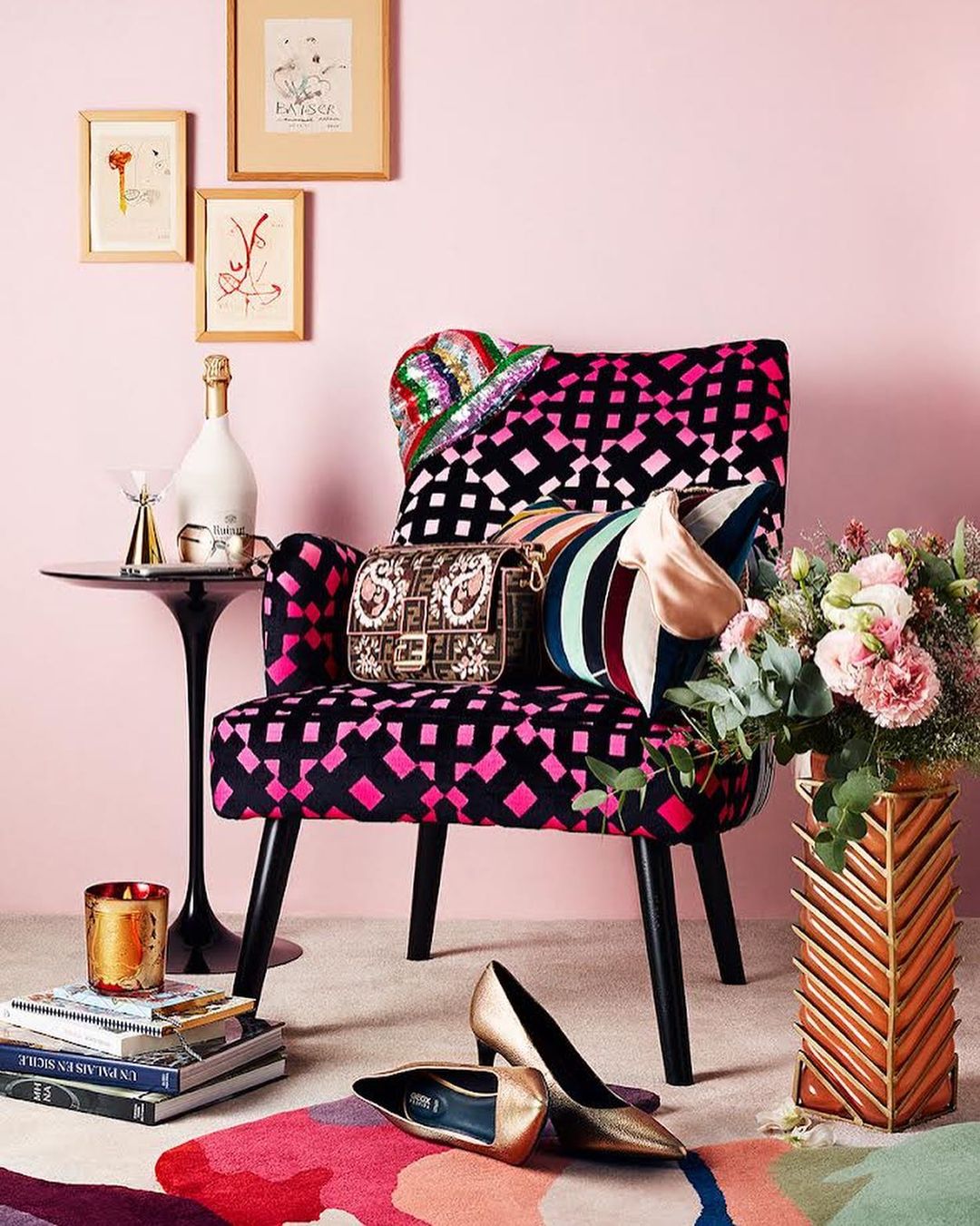 Stylish interior shot featuring a patterned chair adorned with a handbag and hat, alongside flowers, shoes, and art, set against a pink wall.