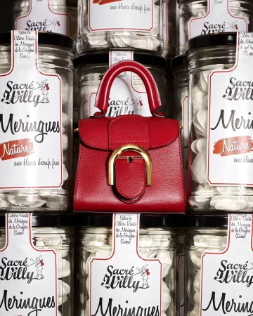 Red Delvaux handbag positioned in front of a stacked display of Sacré Willy Meringues jars, creating a high-fashion, food-themed studio shot.