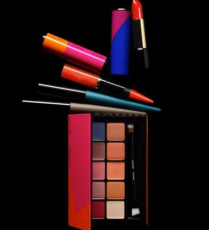 Colorful makeup products including an eyeshadow palette, lipsticks, and eyeliners arranged on a black background.