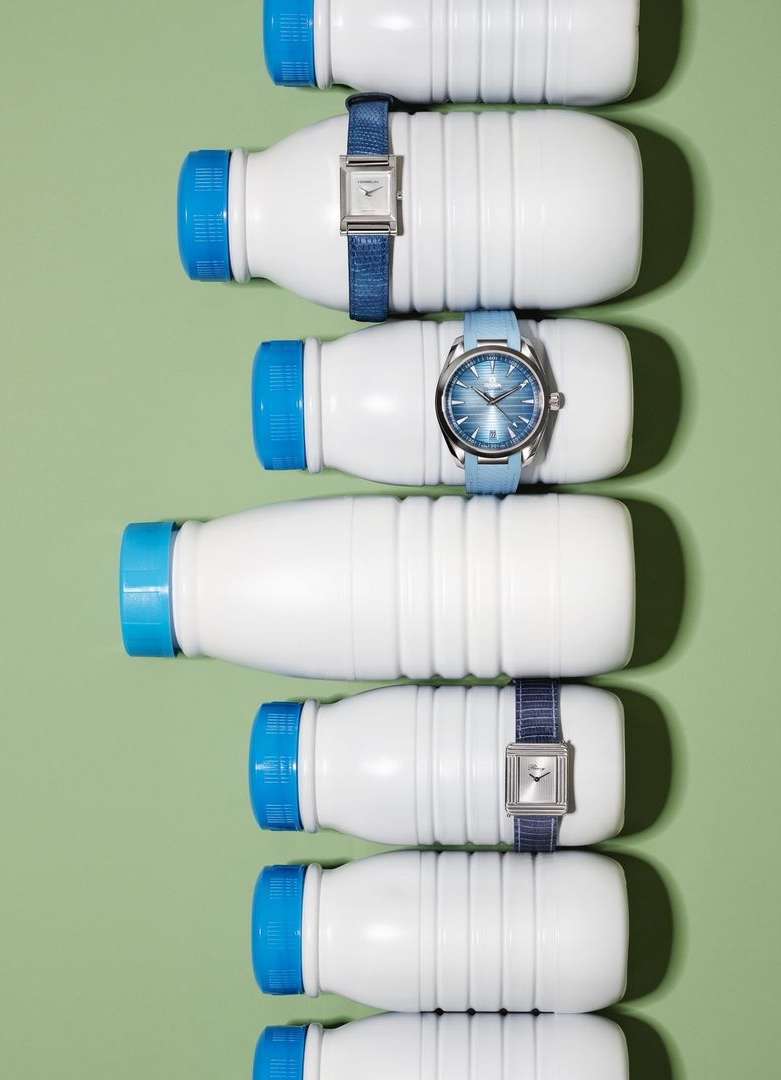 Overhead shot featuring several white bottles with blue caps, each adorned with a blue wrist watch on a light green background.