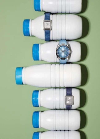 Overhead shot featuring several white bottles with blue caps, each adorned with a blue wrist watch on a light green background.