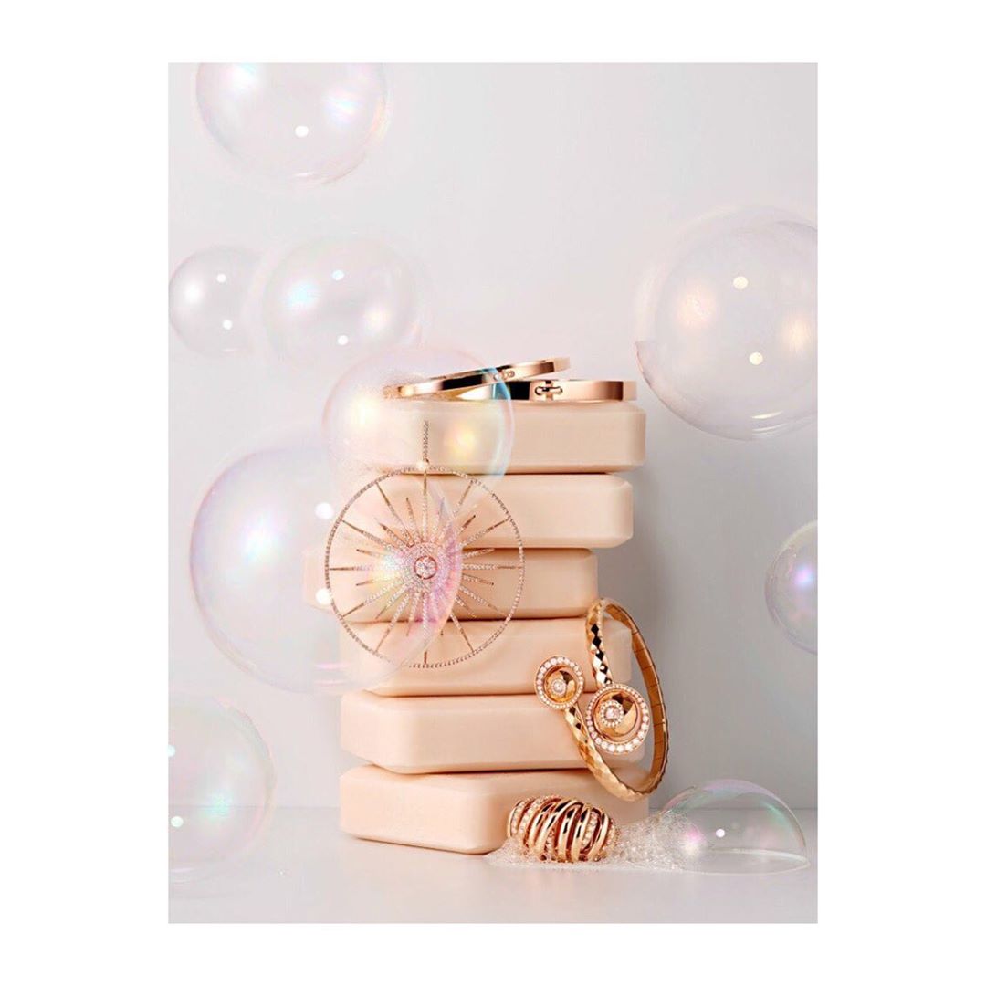 Still life shot of a stacked set of pink soaps and gold jewelry, surrounded by transparent bubbles, creating a luxurious and clean aesthetic.