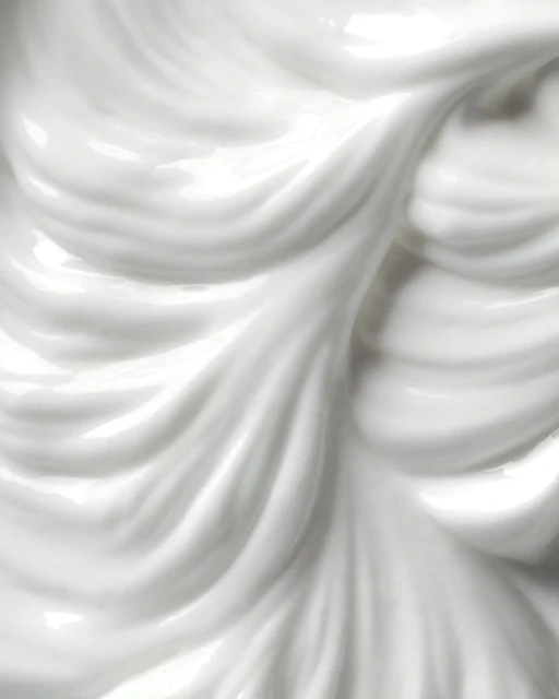 Close-up of glossy white cream with fluid, wavy texture forming smooth peaks and valleys, creating a visually appealing surface.