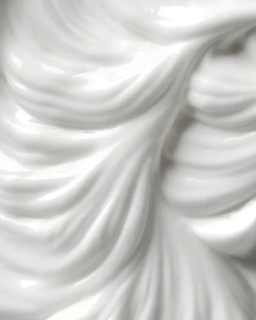 Close-up of glossy white cream with fluid, wavy texture forming smooth peaks and valleys, creating a visually appealing surface.