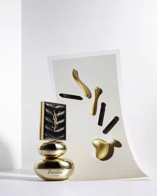 Yves Saint Laurent skincare and makeup products arranged in studio setting with cosmetic applicators, gold accents, and luxury branding.