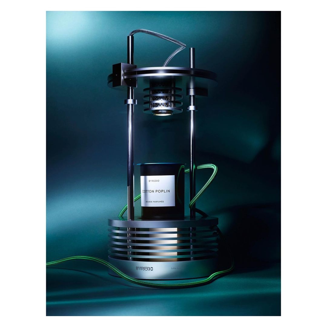 Modern perfume diffuser with a black bottle, silver structure, and glowing light against a dark green background, highlighting design.