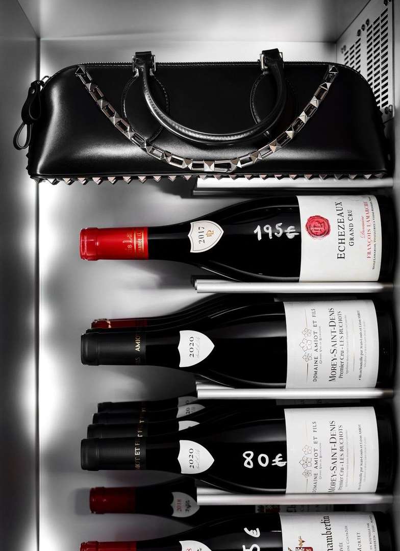 Black leather purse with studded detail and multiple wine bottles in a refrigerated beverage display case for wine and alcohol.
