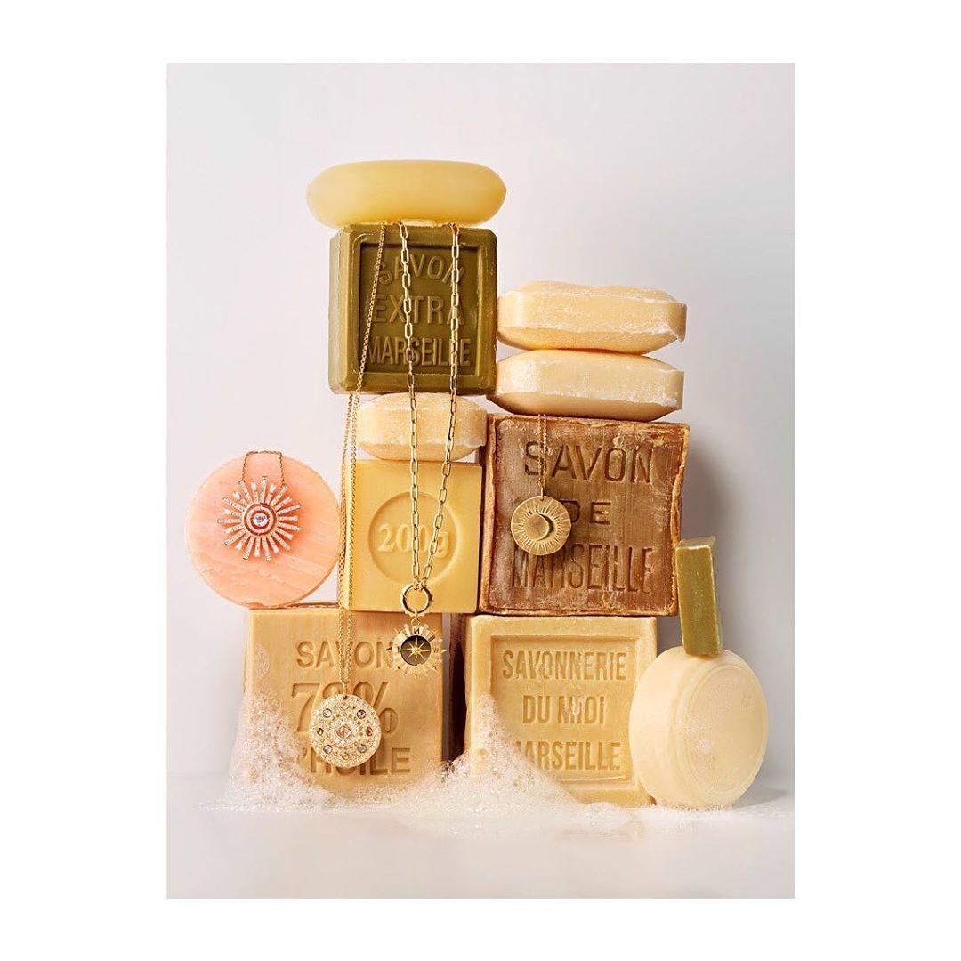 Stacked soaps of varying colors and shapes form a tower, adorned with a gold chain necklace and circular pendants, product shot.