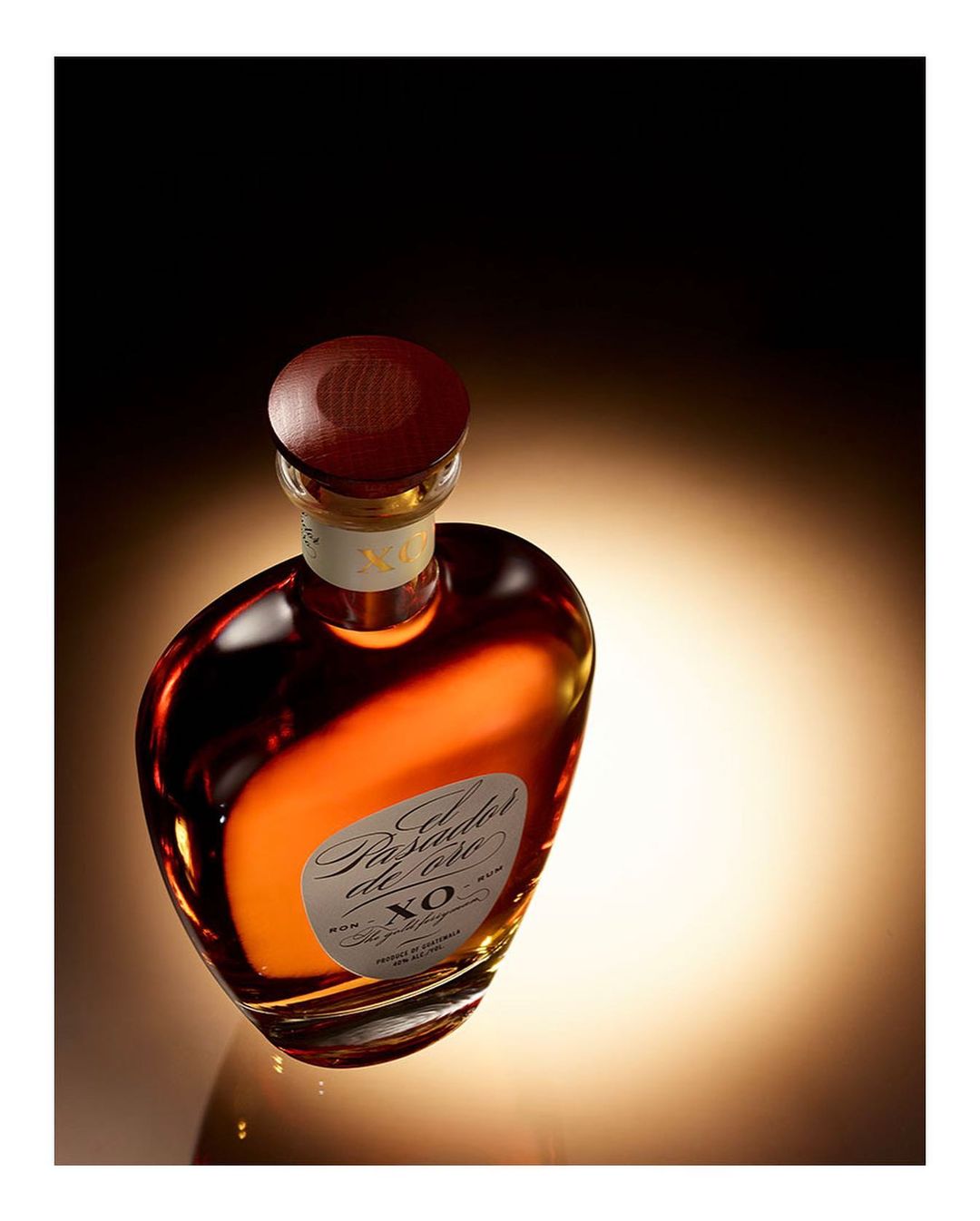 Elegant, aged rum in a stylish glass bottle with a wooden cap, set against a gradient light background in a close-up shot.