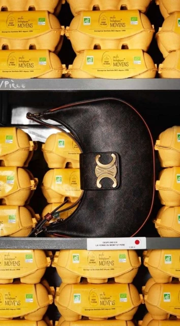 Luxury black leather Celine handbag displayed in front of stacked carton egg boxes. The handbag features gold hardware and a shoulder strap.
