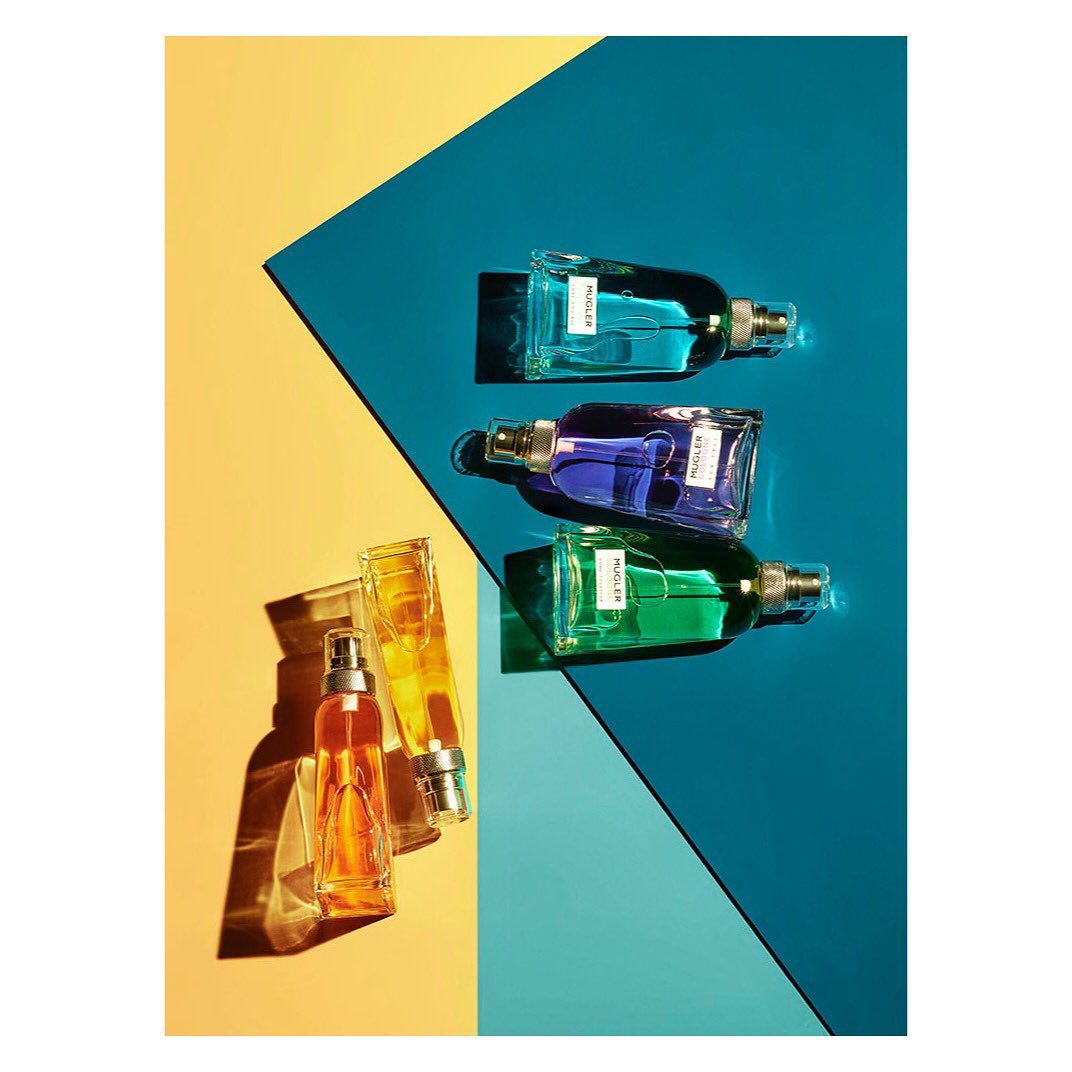 Overhead studio shot: Colorful fragrance bottles lined on contrasting yellow and blue backdrop. Minimalist beauty product photography.