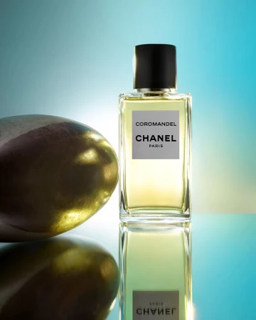 Chanel Coromandel perfume bottle standing next to a smooth golden stone on a reflective cyan gradient surface
