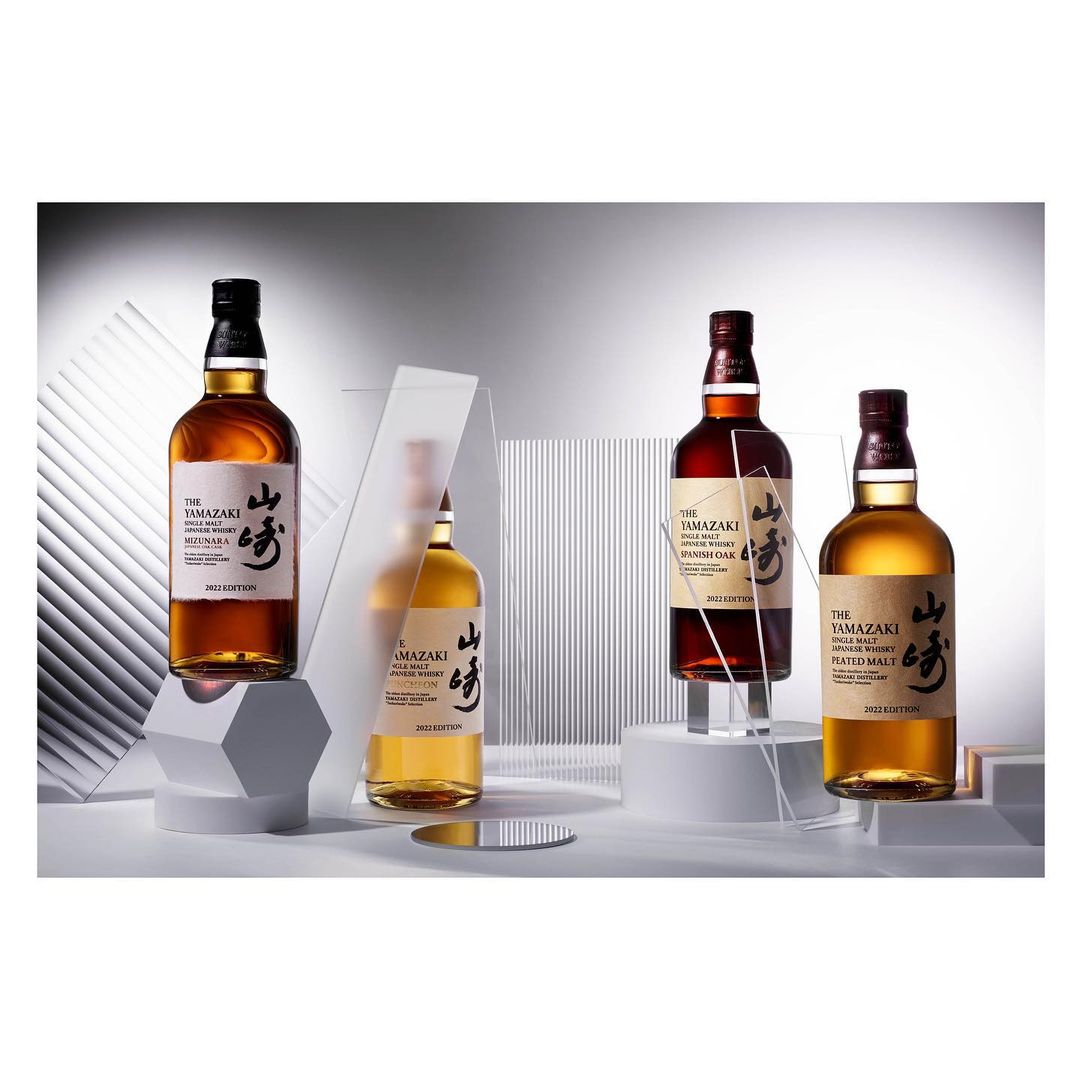 Four bottles of Yamazaki whisky displayed on white platforms with acrylic panels in a product shot for advertisement.