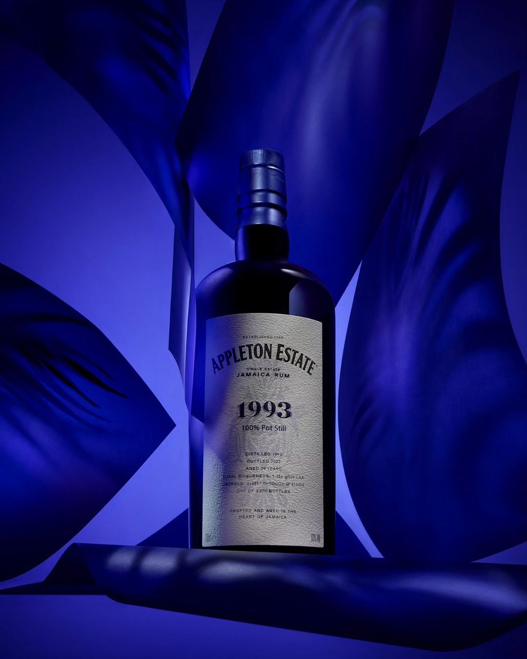 Appleton Estate Jamaica Rum bottle on a blue background. The bottle is dark with a silver label. The background is blue fabric.