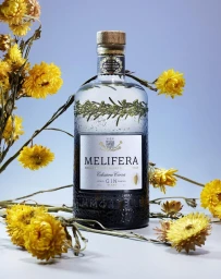 Melifera gin bottle surrounded by yellow strawflowers against a pale grey background