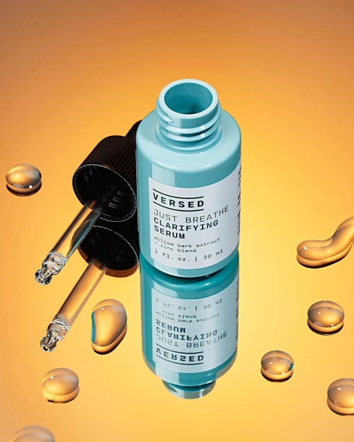Versed clarifying serum bottle with dropper and scattered water droplets on reflective gradient orange surface in a studio setting.