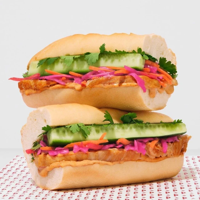 Two appetizing stacked sandwiches featuring fresh cucumber slices, cilantro, and red cabbage on a white surface with a patterned background.