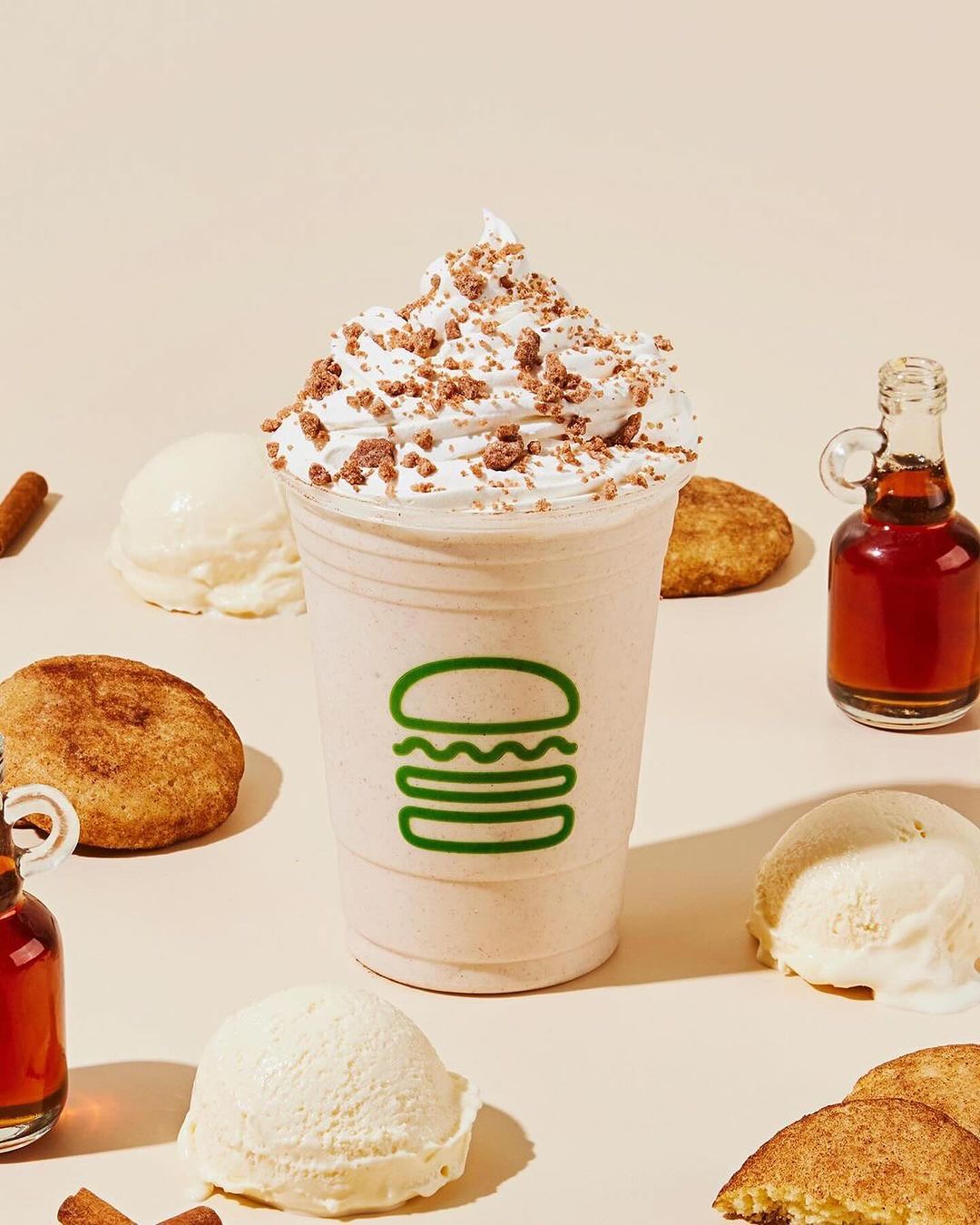A milkshake with whipped cream and sprinkles, accompanied by scoops of vanilla ice cream, cookies, and bottles of syrup.