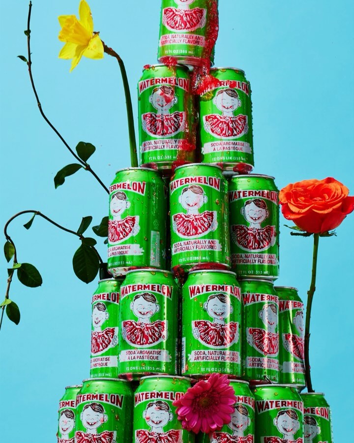 Tower of green watermelon soda cans, stacked with pink, yellow, and orange flowers against a blue background for product display.