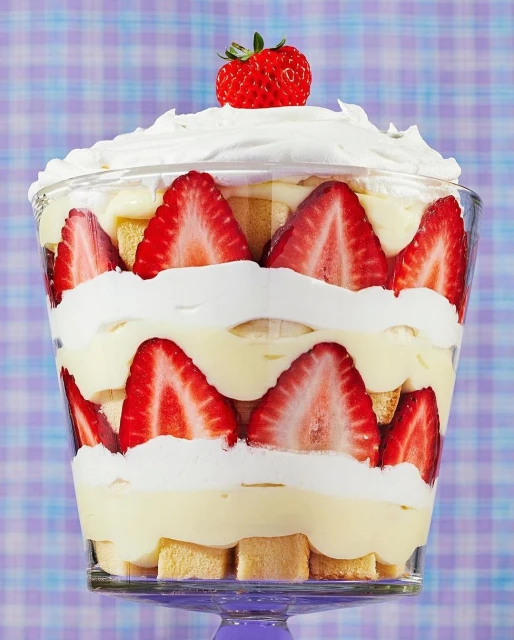 Close-up of a trifle dessert in a clear glass with layers of strawberries, pastry cream, whipped cream and garnished with a strawberry.