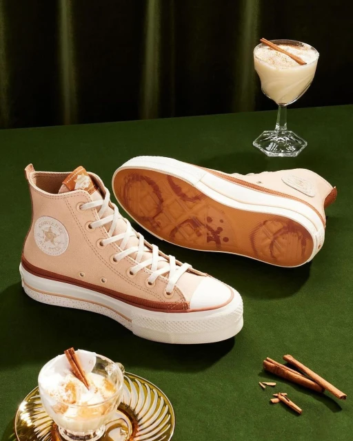 Pair of platform Converse sneakers are staged near two dessert cocktails garnished with cinnamon sticks, against a green background.
