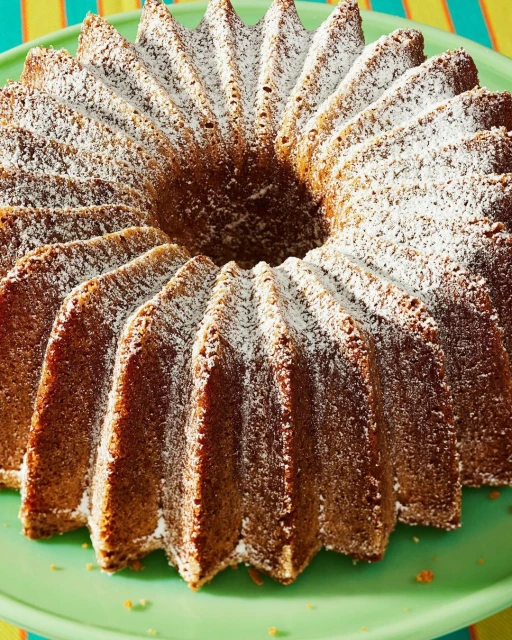 Bundt cake covered in powdered sugar on a green cake stand, with a colorful striped background out of focus.