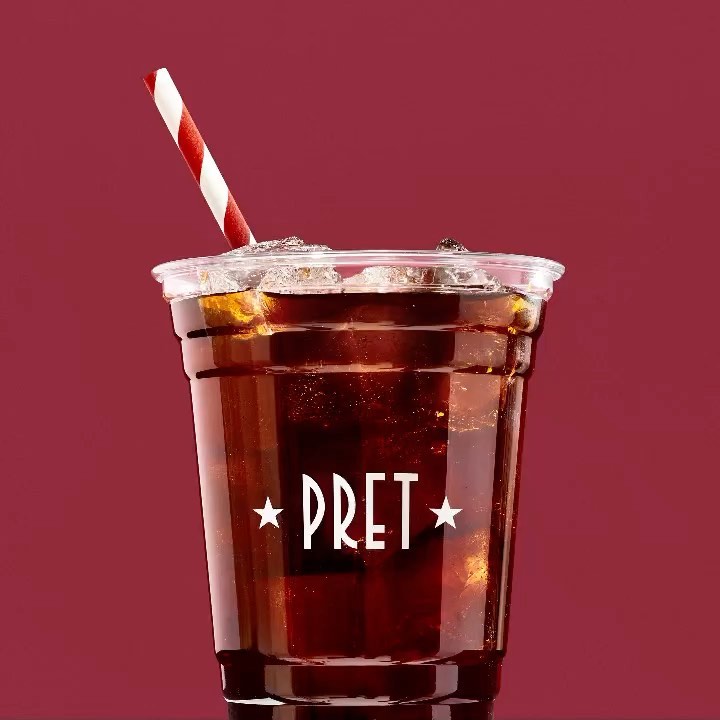 Iced drink in a clear plastic cup with a red and white striped straw on a maroon background, 'PRET' logo on the cup.