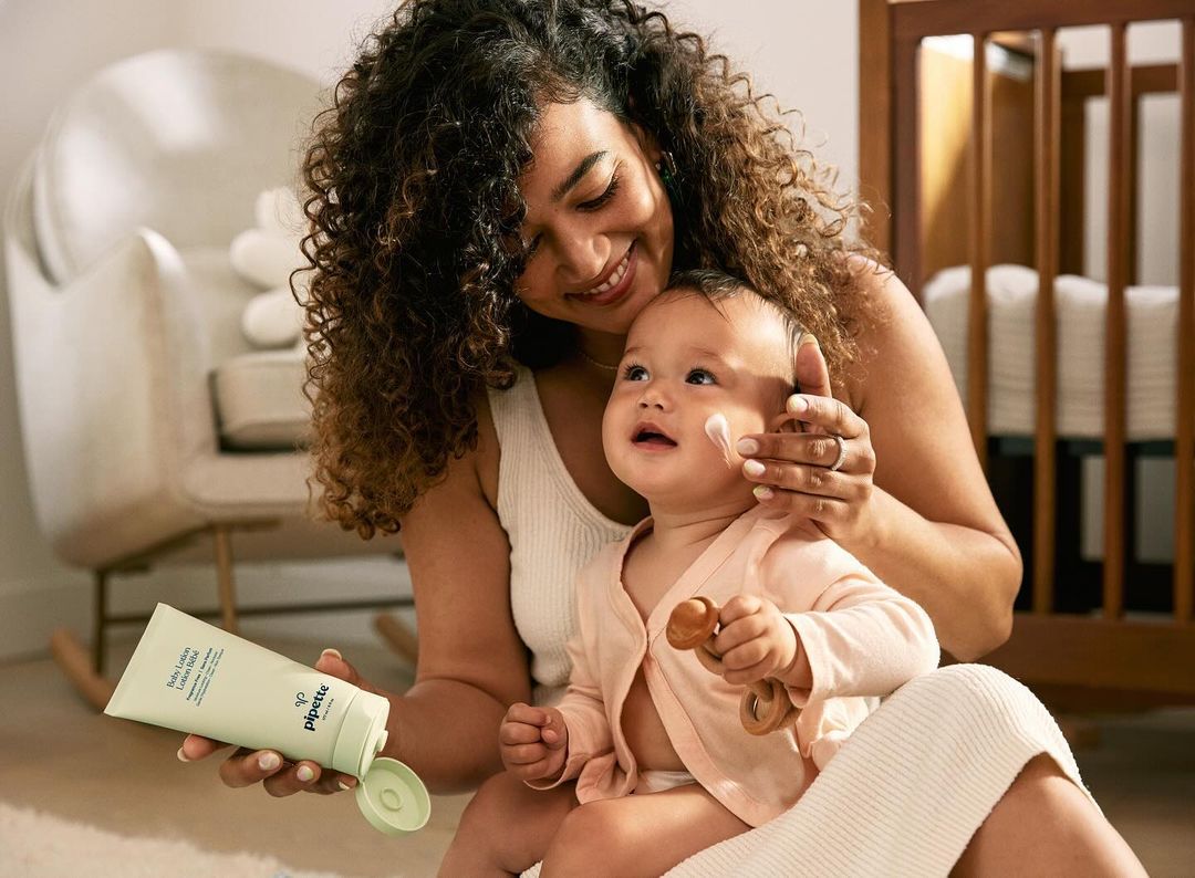 Mother and child in indoor setting. The mother is holding a lotion bottle. Cream is applied to the child's face.