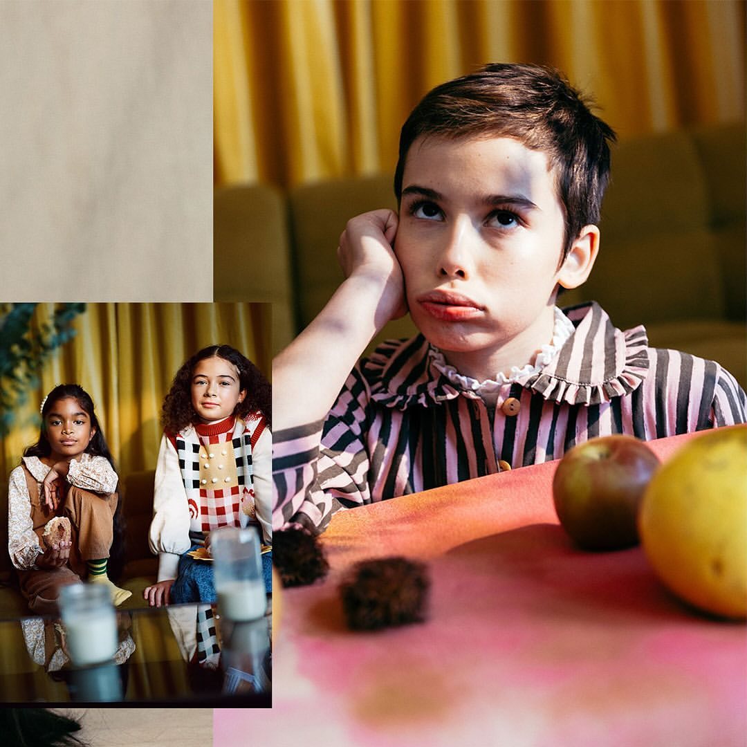 Portrait of a child in striped pajamas with a sullen expression, sitting at a table with fruit, with other children in background.