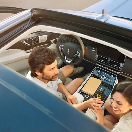 A couple sits inside a convertible Lincoln car with a tan notebook and flower on the console, capturing a moment of automotive elegance.