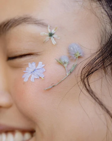 Close-up portrait of a woman with small pressed flowers delicately adhered to her face, photographed by Emily Hlavac Green.