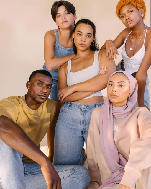 Group portrait of five diverse young adult friends posing in casual neutral fashion against a light-beige backdrop in a photo studio.
