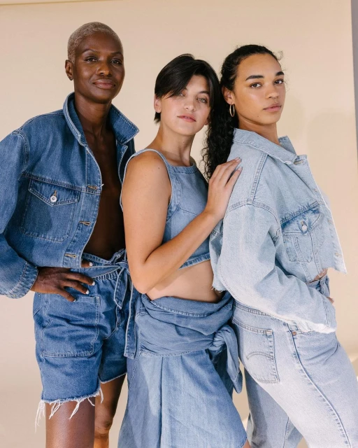 Three diverse women in denim outfits pose in a studio setting, showcasing various denim styles and textures under neutral lighting.
